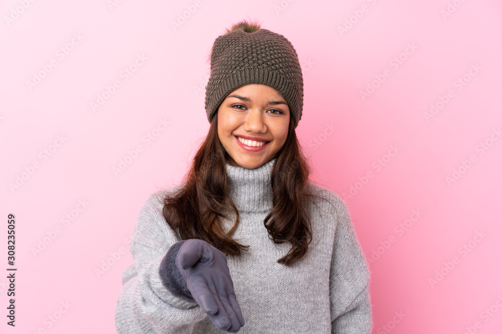 Young Colombian girl with winter hat over isolated pink wall handshaking after good deal Young Colombian girl with winter hat over isolated pink wall handshaking after good deal