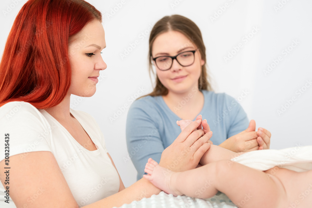 Female massage therapist teaching young mother how to massage her newborn baby boy. Baby massage concept. Female massage therapist teaching young mother how to massage her newborn baby boy. Baby massage concept.