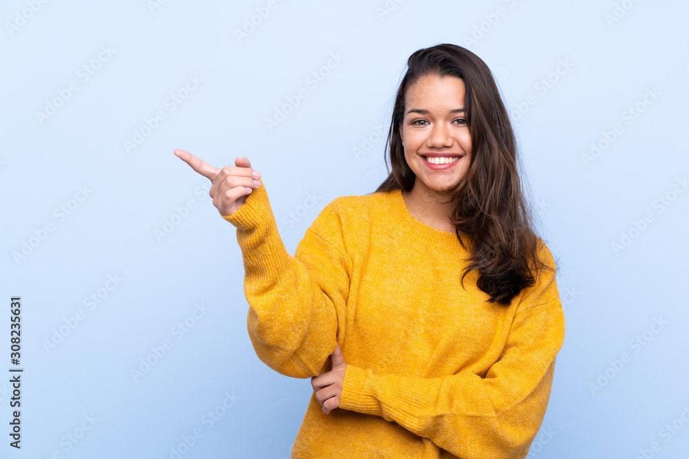 Young Colombian girl with sweater over isolated blue background pointing finger to the side Young Colombian girl with sweater over isolated blue background pointing finger to the side