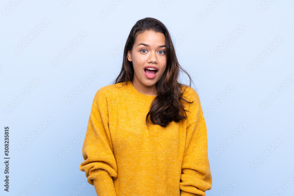 Young Colombian girl with sweater over isolated blue background with surprise facial expression Young Colombian girl with sweater over isolated blue background with surprise facial expression