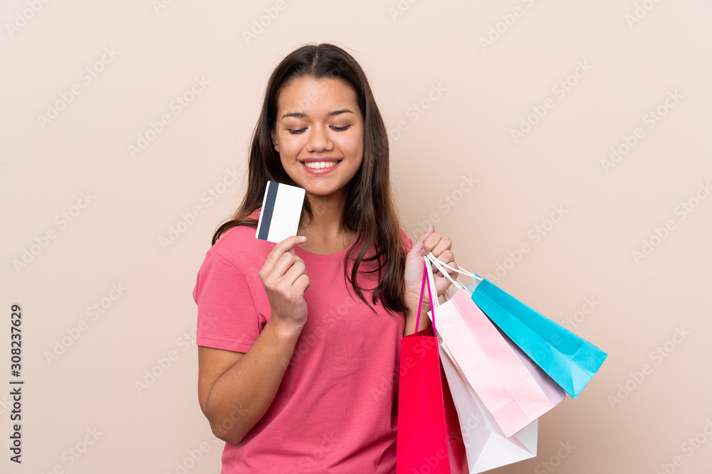 Young Colombian girl with shopping bag over isolated background holding shopping bags and a credit card Young Colombian girl with shopping bag over isolated background holding shopping bags and a credit card