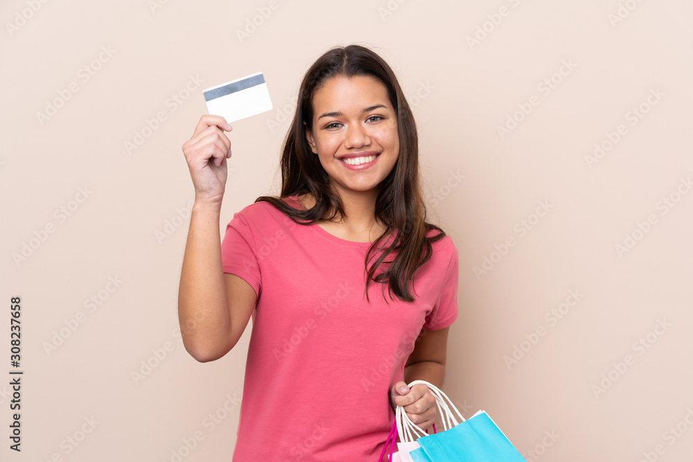Young Colombian girl with shopping bag over isolated background holding shopping bags and a credit card Young Colombian girl with shopping bag over isolated background holding shopping bags and a credit card