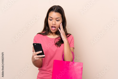 Young Colombian girl with shopping bag over isolated background holding shopping bags and writing a message with her cell phone to a friend © luismolinero