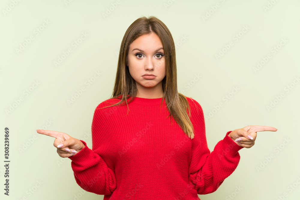Teenager girl over isolated green background pointing to the laterals having doubts Teenager girl over isolated green background pointing to the laterals having doubts