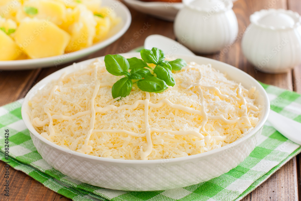 Puff salad with chicken and cheese under mayonnaise on a white plate, selective focus Puff salad with chicken and cheese under mayonnaise on a white plate, selective focus