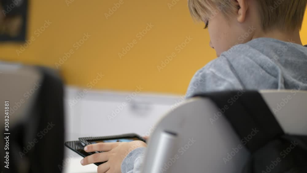 Rear view of caucasian school boy studying on tablet in classroom, Static