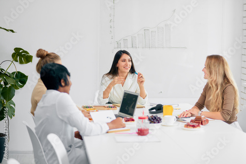 Young business ladies interacting during coffee break at business conference in white office, fruits and cup of tea on table. women colleague gathered to discuss business strategy