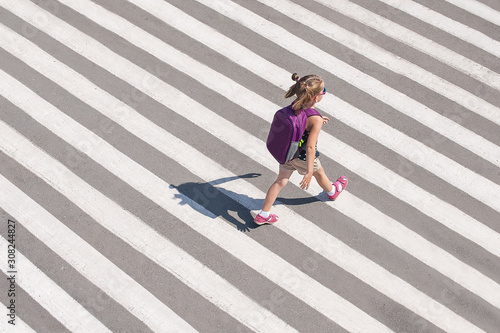 Schoolgirl crossing road on way to school. Zebra traffic walk way in the city. Concept pedestrians passing a crosswalk. Stylish young teen girl walking with backpack. Active child. Top view