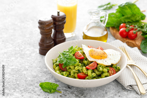 Pasta сavatappi with spinach pesto, tomatoes and fried egg in bowl served for lunch