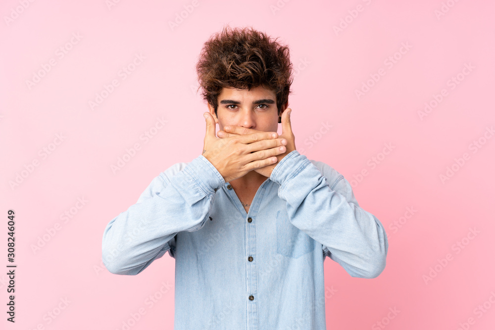 Young caucasian man with jean shirt over isolated pink background covering mouth with hands Young caucasian man with jean shirt over isolated pink background covering mouth with hands