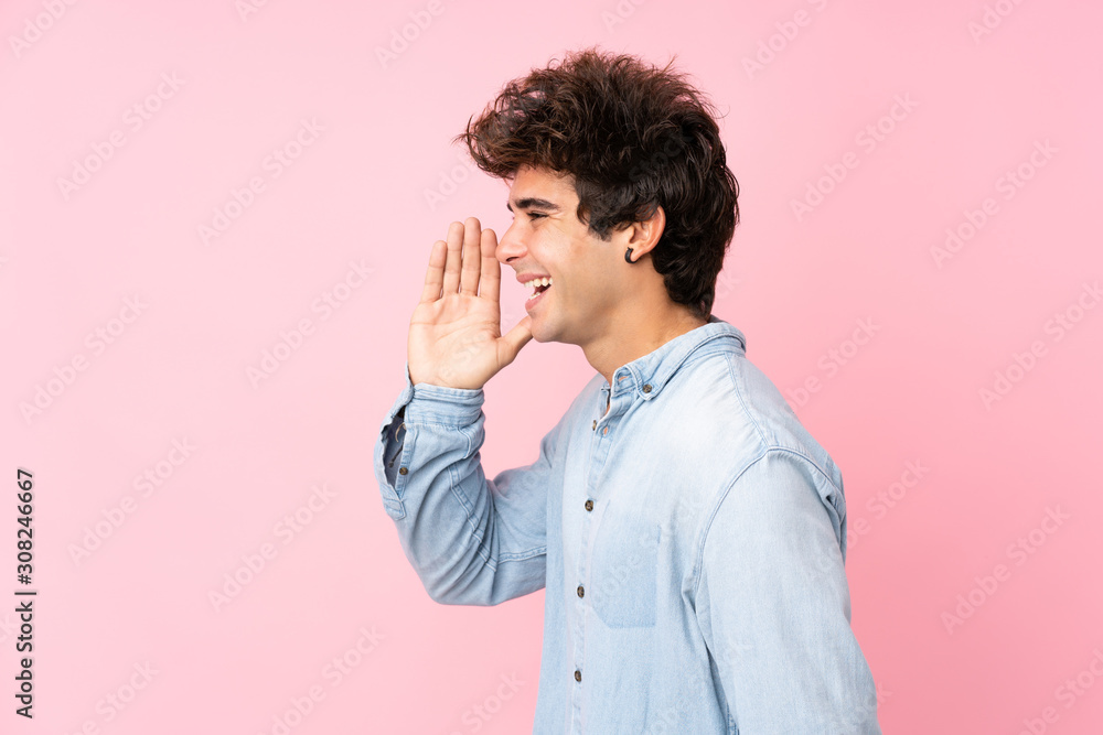 Young caucasian man with jean shirt over isolated pink background shouting with mouth wide open to the lateral Young caucasian man with jean shirt over isolated pink background shouting with mouth wide open to the lateral