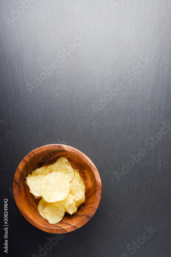 Crispy potato chips in woodenbowl on dark stone background