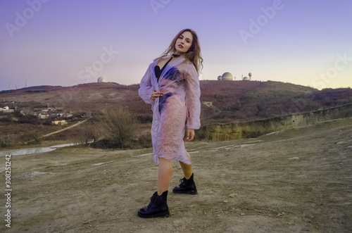Silhouette of a young and sexy girl. She stands on a mountain and poses, dressed in a cloak and black boots against the sunset. Happy celebration victory success woman