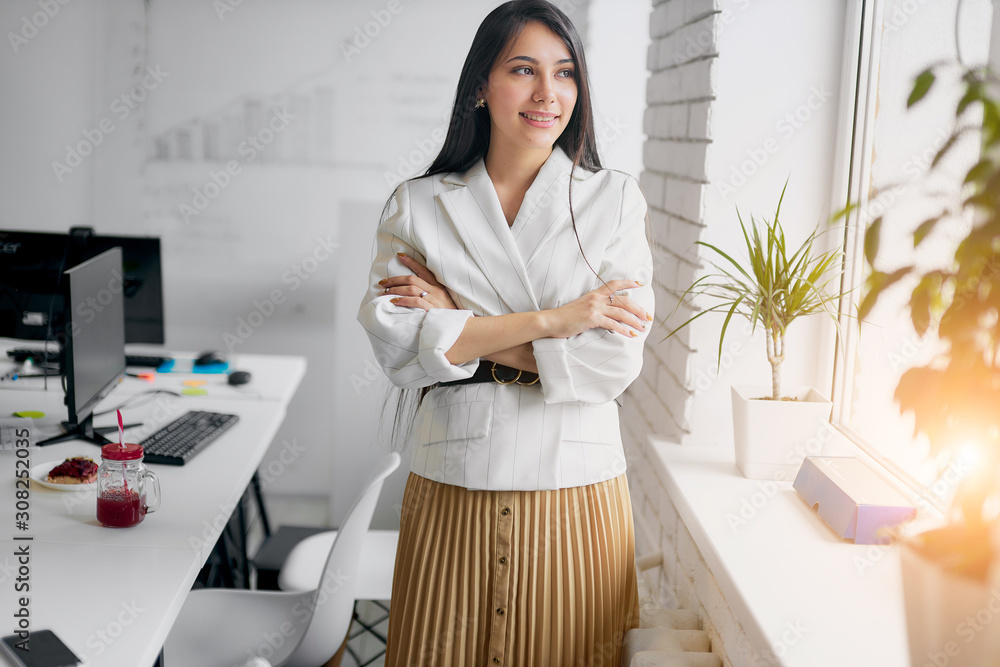 Confident and beautiful woman in formal white wear stand looking side on window in modern white office, posing. Business people concept Confident and beautiful woman in formal white wear stand looking side on window in modern white office, posing. Business people concept