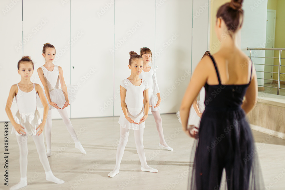 young trainer of the ballet school helps young ballerinas perform different choreographic exercises in studio. children girls rehearse together in the ballet class