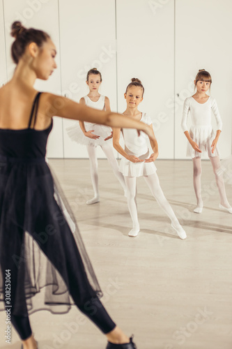 attractive and beautiful caucasian woman wearing black tutu skirt show right poses in ballet to little kids, performing ballet dance in studio, isolated in ballet school