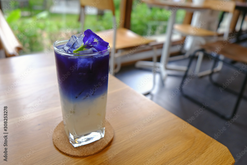 Fresh Asian pigeonwings juice over coconut milk with ice in glass on wood table Fresh Asian pigeonwings juice over coconut milk with ice in glass on wood table