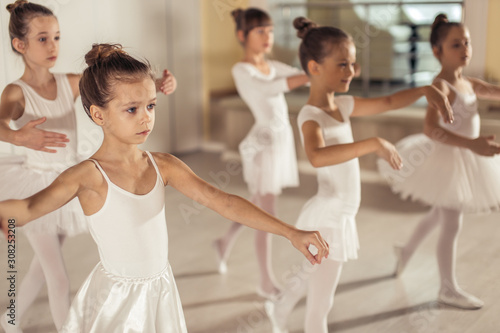 little kids ballerinas in studio, wearing white tutu skirts, stand in pose, performing classic ballet dance, smooth movements