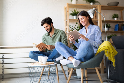 Happy young couple relaxing. Reading something on book and tablet computer. photo