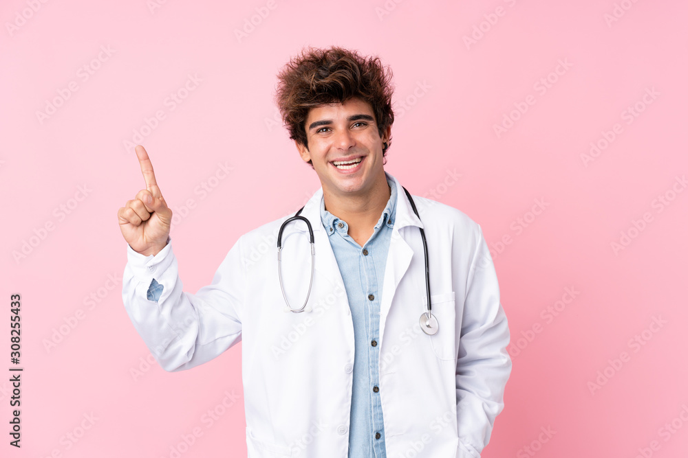 Young caucasian man over isolated pink background with doctor gown and pointing side