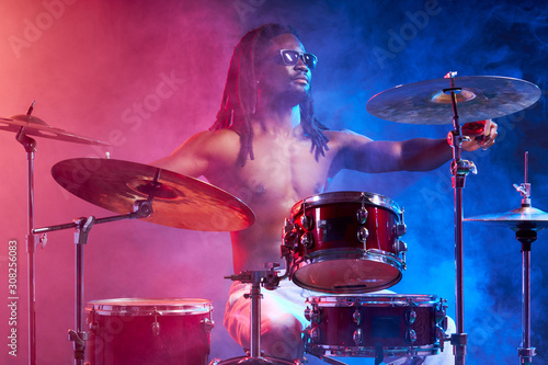 awesome black man with naked skin playing on drums  isolated over neon smoky background