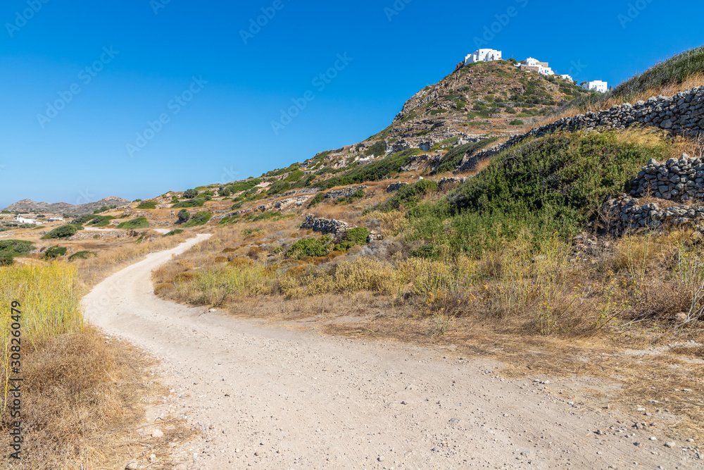 Dirty road with rocks and vegetation and Plaka village Dirty road with rocks and vegetation and Plaka village