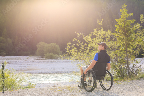 Happy and joyfull young man in wheelchair outside in nature on a sunny summer day with his hands raised up.