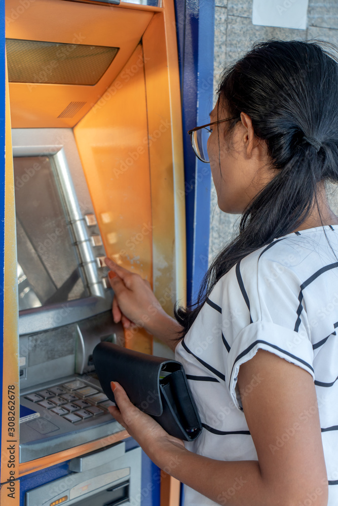 Fotografie Young woman with wallet standing by ATM