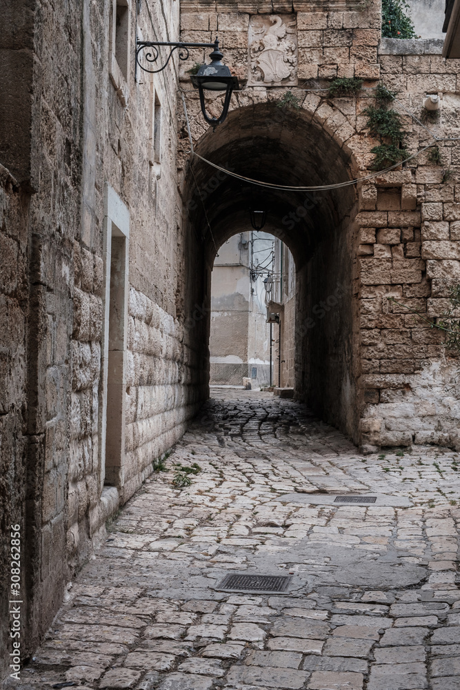 Narrow street in the old town, stone walls, arched passage, lantern. Monopoli, Italy.