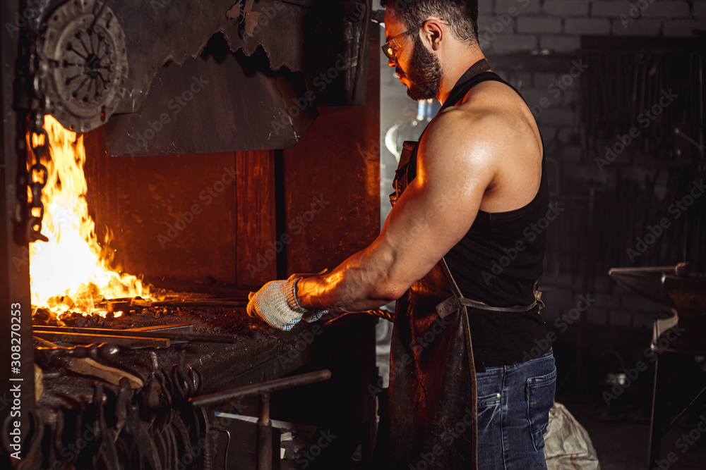 handsome muscular caucasian man with strong muscles on hands, side view on man opposite the fire, wearing eyeglasses for safety handsome muscular caucasian man with strong muscles on hands, side view on man opposite the fire, wearing eyeglasses for safety