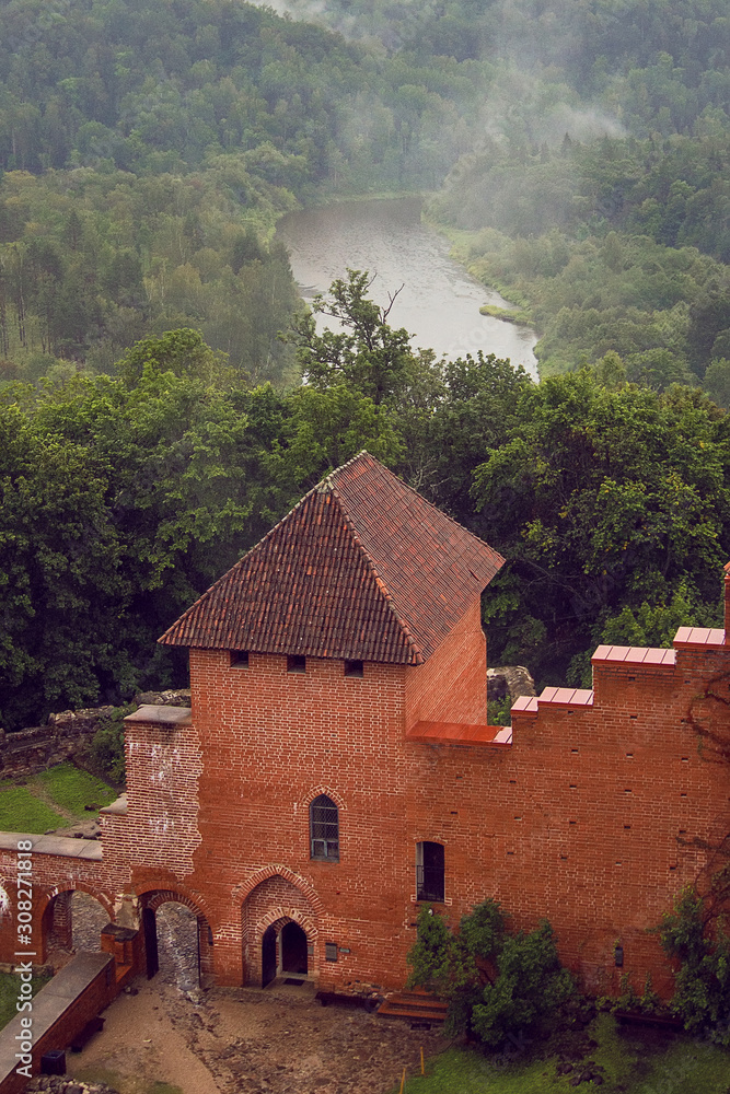 Aerial view on the red brick gate to the courtyard of medieval Turaida Castle from the main big tower in cloudy, foggy and rainy day, Sigulda, Latvia. Soft focus