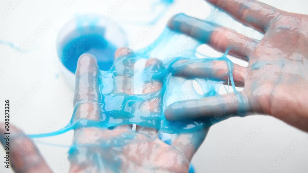 Girl stretching blue slime to the sides. Woman hands playing slime toy. Making slime on white. Trendy liquid toy sticks to hands and fingers. 4k footage. Girl stretching blue slime to the sides. Woman hands playing slime toy. Making slime on white. Trendy liquid toy sticks to hands and fingers. 4k footage.