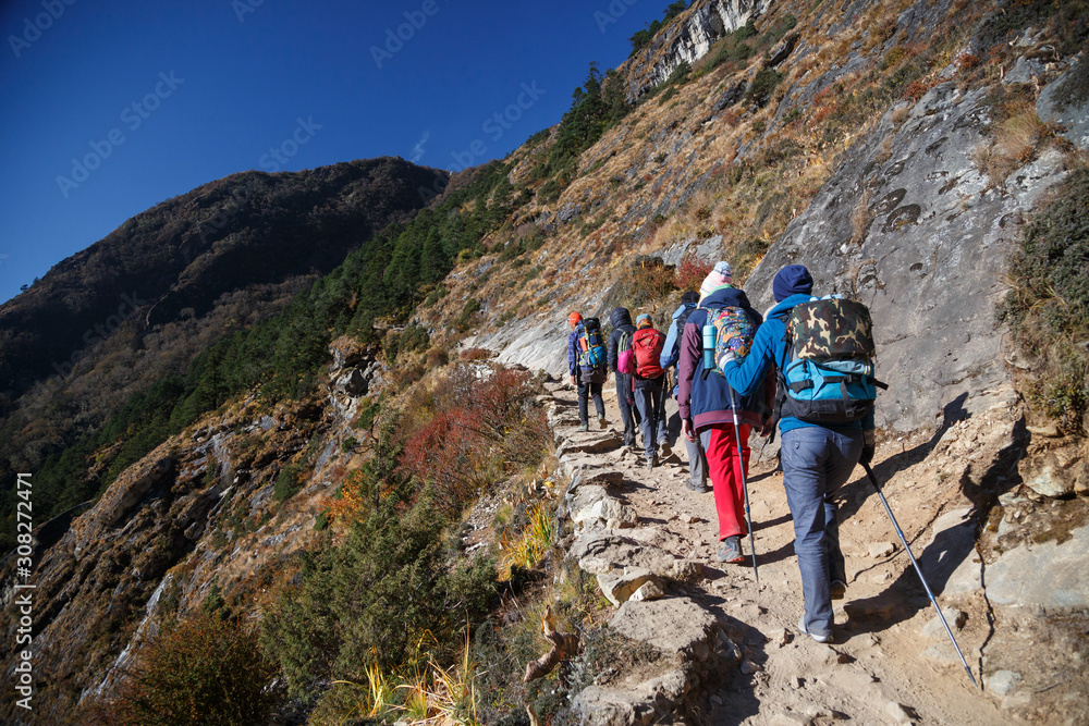 Fototapeta premium Travellers follow a narrow path on a mountainside. Bright sunny day. Nepal. 