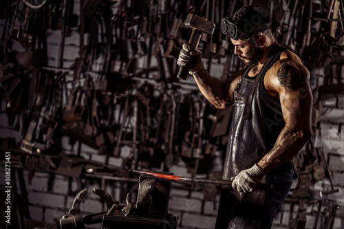 muscular man work at workshop using hammer, wearing leather uniform and having strong body