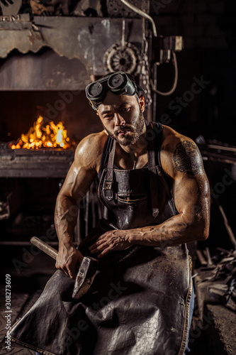 portrait of strong muscular blacksmith man wearing black apron, look confidently, have strong powerful hands and shoulders. © alfa27