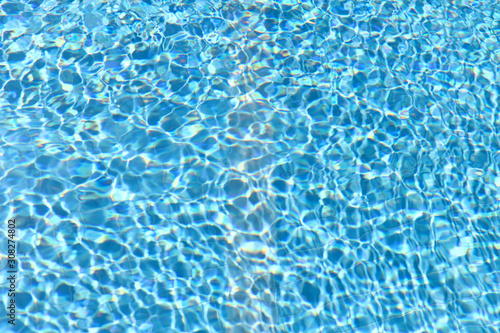 Background texture of the pool water. Reflection of sunlight in the pool water. Horizontal, close-up, cropped shot. The concept of sports and recreation.