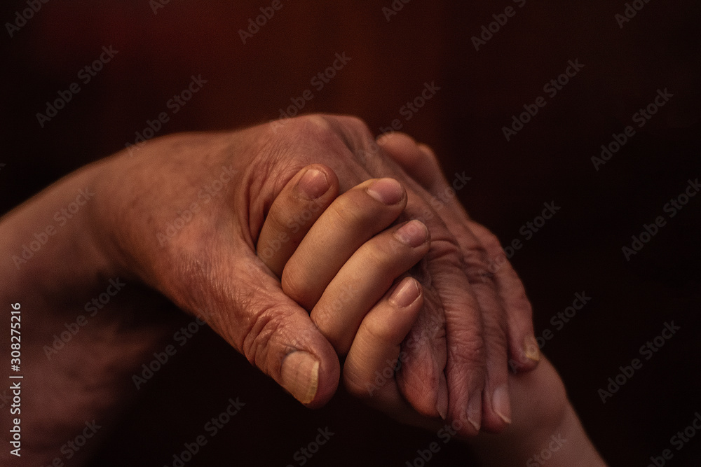 The hands of an old grandmother and a child touch in a handshake for support and help.