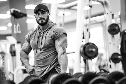 sport training motivation concept young active strong athlete male with beard posing before mirror in fitness gym club with sports equipment