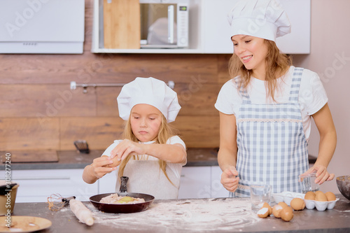 daughter help mother to cake, bake. prepare dough for tasty delicious cake, wearing aprons and special caps. isolated in kitchen