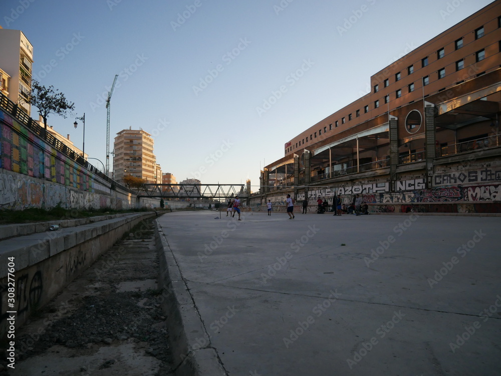 People playing volleyball in the dry riverbed of the Guadalmedina river in Málaga, Spain, with just a few small streams or puddles of water on the concrete ground and grass