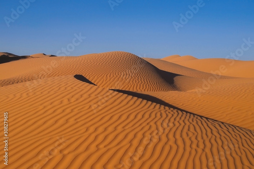 the sahara desert with red sand and beautiful wave pattern and blue sky