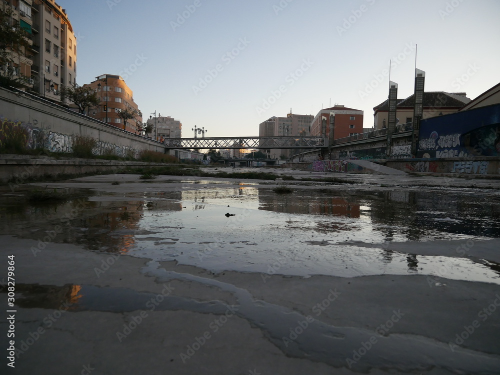 Dry riverbed of the Guadalmedina river in Málaga, Spain, with just a few small streams or puddles of water on the concrete ground and grass