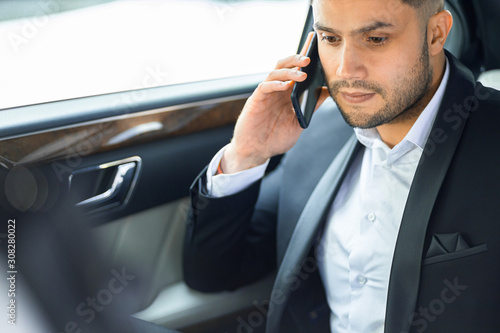 close-up of personable successful man wearing formal wear use smartphone for talking with business partners, solving problems while sitting in car