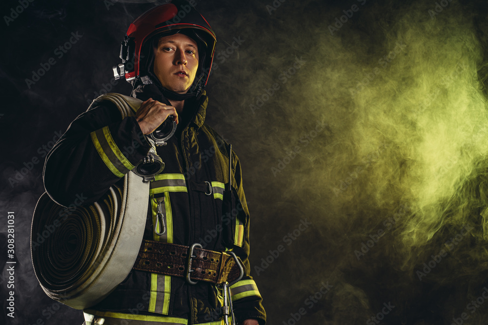 brave extinguisher or fireman dressed in dark protective suit uniform, with helmet on head, using ropes, hammer and other special equipment at work brave extinguisher or fireman dressed in dark protective suit uniform, with helmet on head, using ropes, hammer and other special equipment at work
