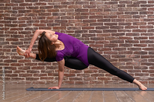 Beautiful woman with slender body doing yoga in on a brick wall background