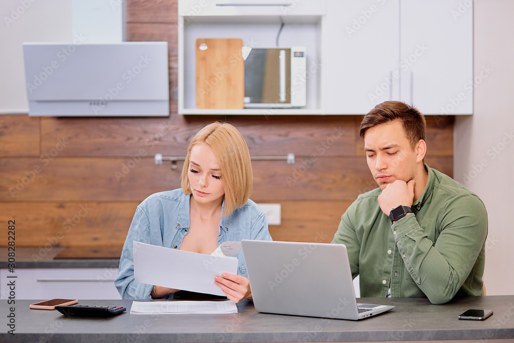 young caucasian woman and man wearing casual wear checking financial situation in family, doing invoice verficitaion using laptop, papers and calculator young caucasian woman and man wearing casual wear checking financial situation in family, doing invoice verficitaion using laptop, papers and calculator