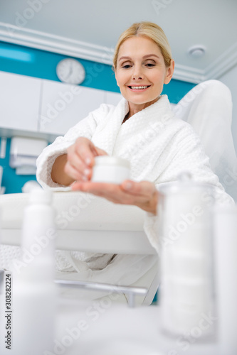 Happy adult woman holding cream in beauty salon