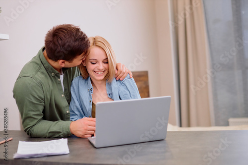 awesome beautiful lovely couple sit together on table at home using laptop, man want to kiss woman, love, family concept