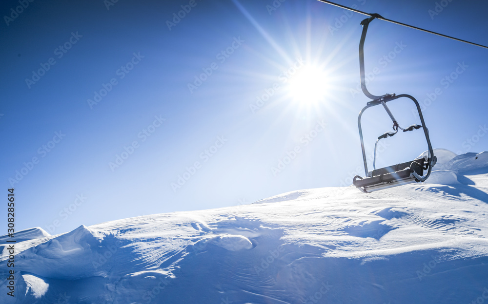 Ski lift seats high in the mountains. Winter elevator mountains panorama with sun and blue sky in background. Copy space for text.