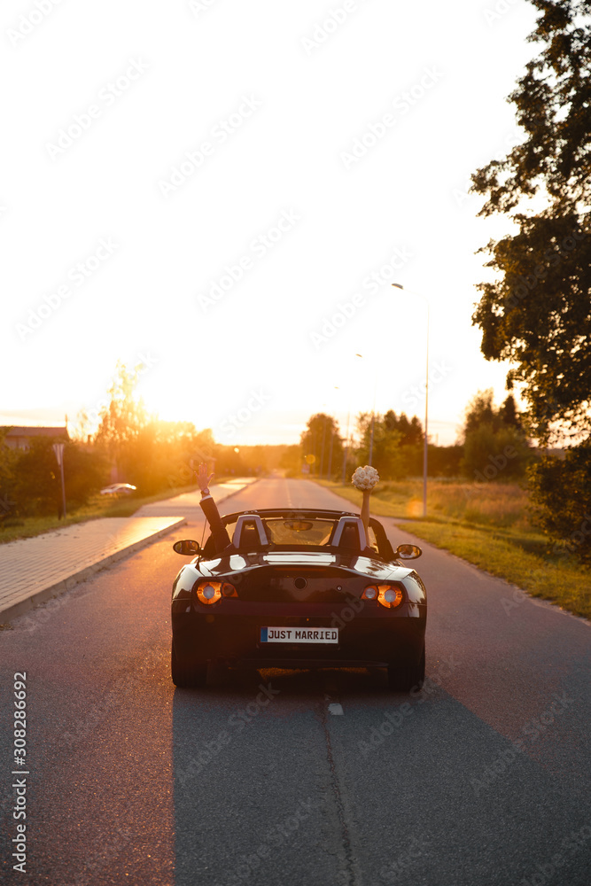 Wedding Just Married sign black rodster cabrio coupe car with bride and groom leaving into sunset in Eastern European Baltic Riga Latvia